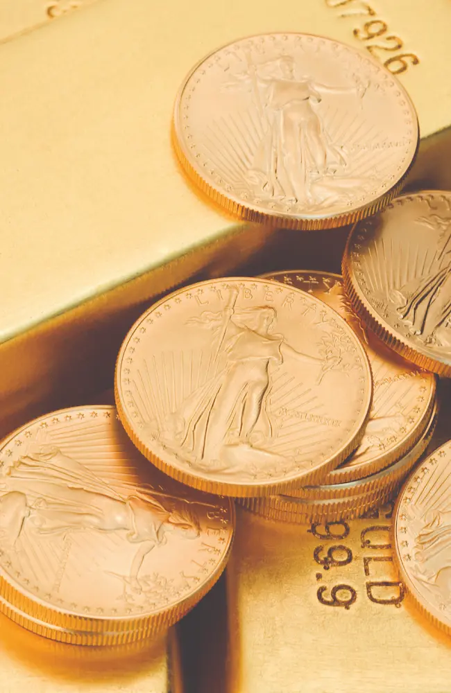 Gold bullion bars and coins layed on top of them.